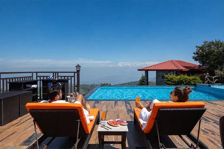 Couple relaxing by an infinity pool overlooking the Himalayan mountains at a luxury resort in Mukteshwar.