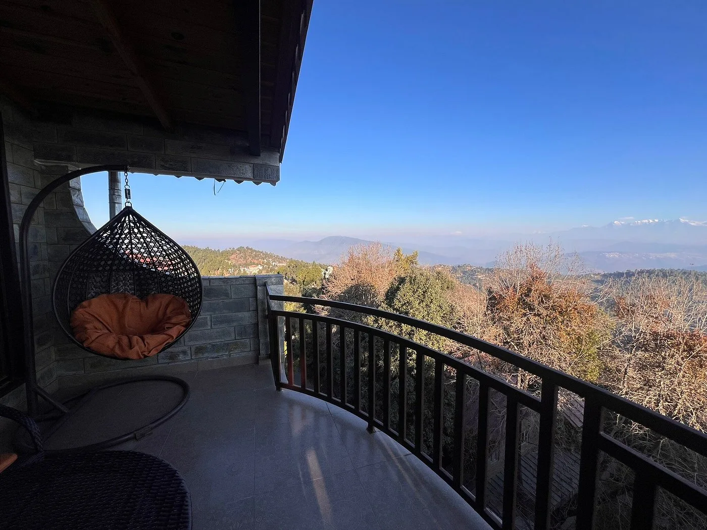 Balcony with a hanging egg chair overlooking hazy hills and distant snow-capped peaks.