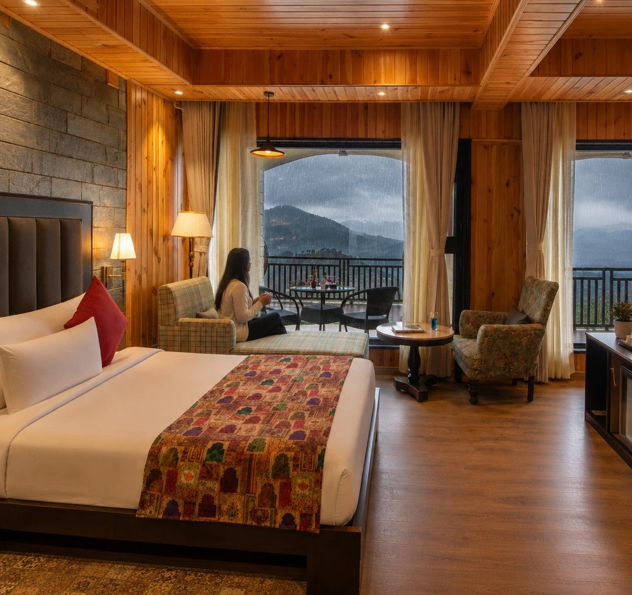 Woman watching rain over misty mountains from a wood-paneled suite.