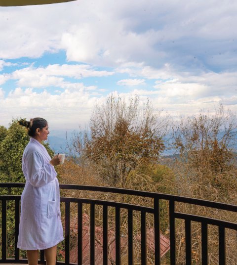 Guest enjoying a peaceful morning coffee on the balcony at Ojaswi Resort in Mukteshwar with scenic Himalayan views