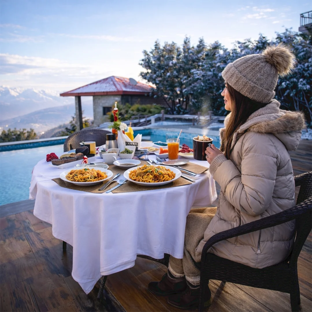 Woman having breakfast poolside with snow-capped mountains in the distance