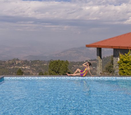 A guest relaxing at the edge of the infinity pool at Ojaswi Resort, taking in the expansive mountain landscape.